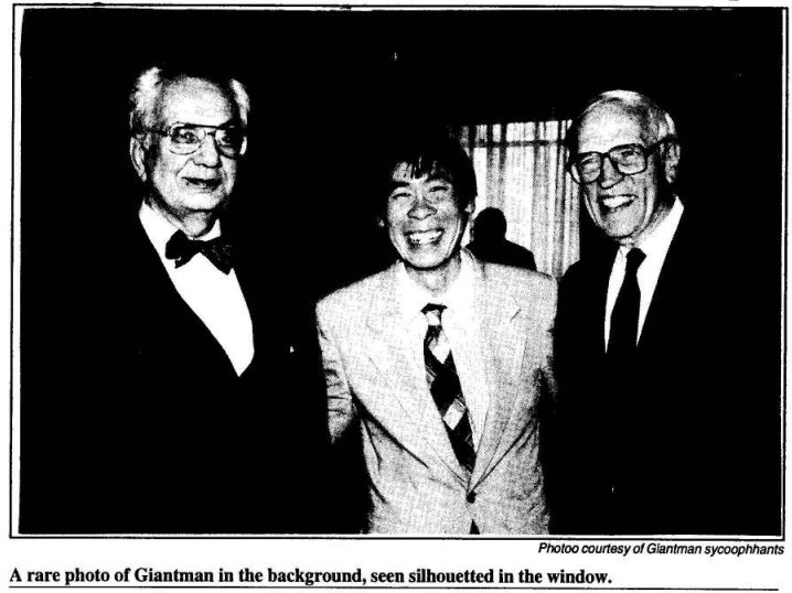 Black and white photo of three men smiling in front of a window with a dark silhouette. The caption of this photo reads "A rare photo of Giantman in the background, seen silhouetted in the window. Photo courtesy of Giantman sycophants." The Tufts Daily, 10 November 1994.