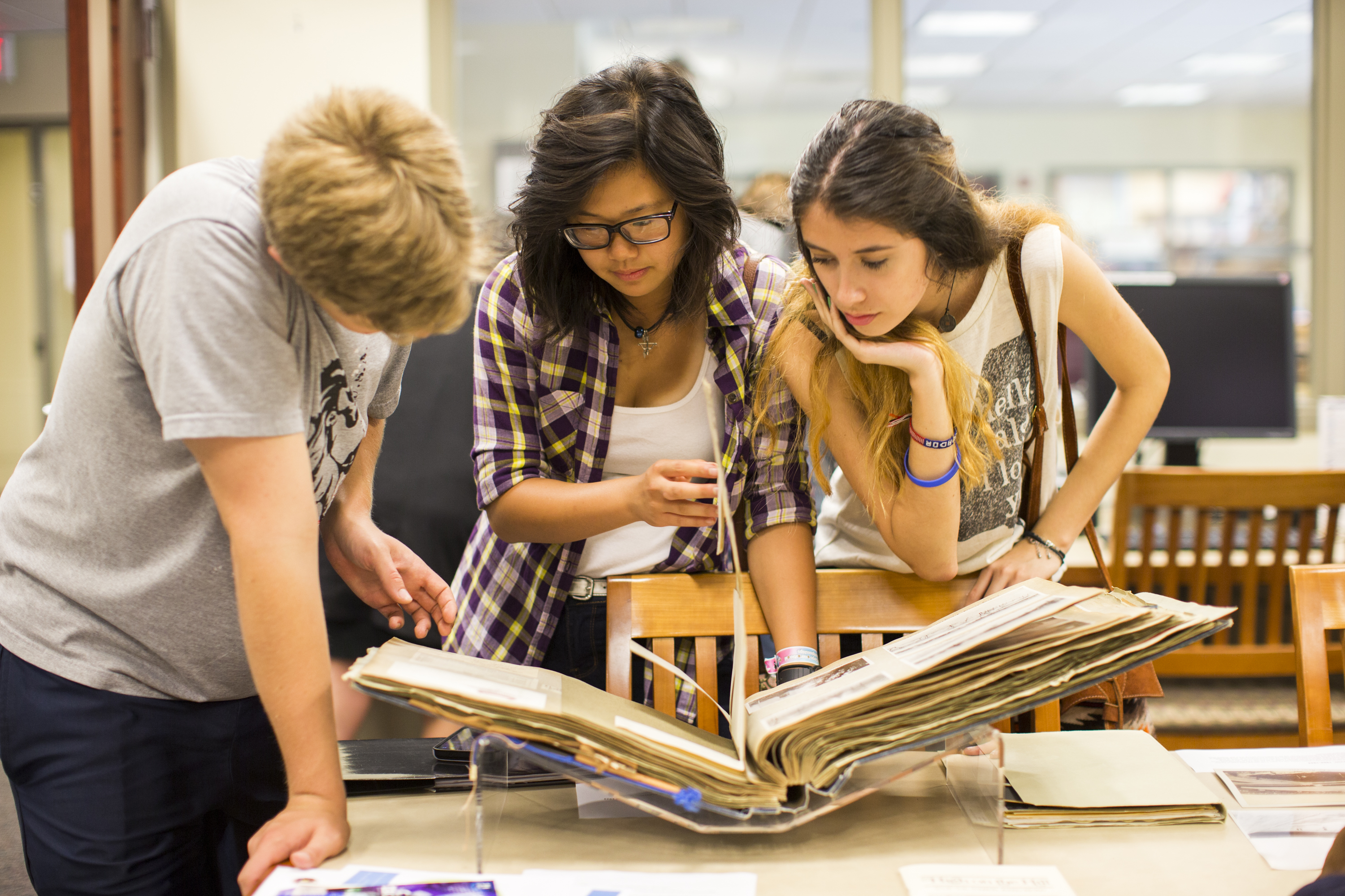Color photo of three students viewing a scrapbook in the TARC Reading Room.