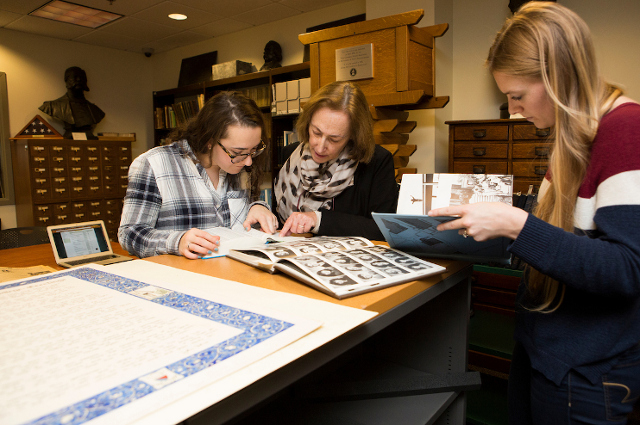 Color photo of a faculty member and two younger women working with archival materials.