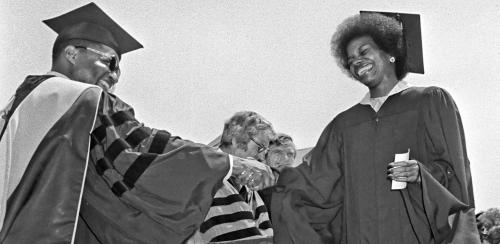 Black and white photo of Dean Harleston greeting a graduate as she accepts her diploma.