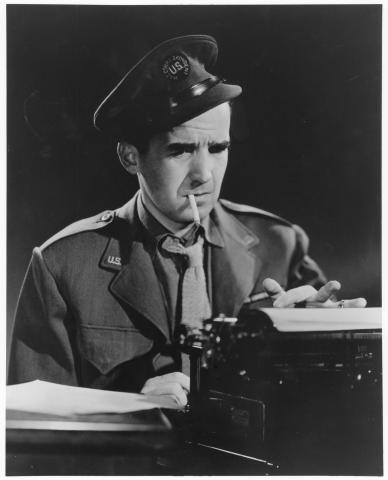 Black and white image of Edward R. Murrow sitting at a typewriter and smoking a cigarette in a military uniform.