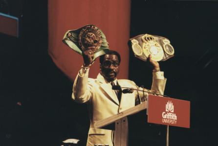 Rubin Carter holding his championship belts at a speaking engagement.